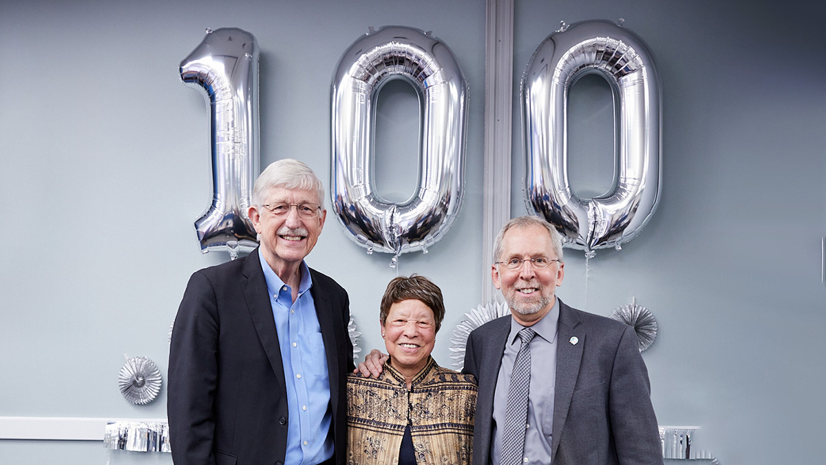 Bettie Graham (center) with Francis Collins (left) and Eric Green (right) pose for a picture in front of 100th Council Anniversary balloons