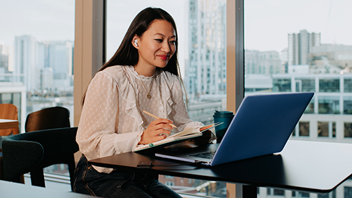 A young professional takes notes as she looks at her laptop.